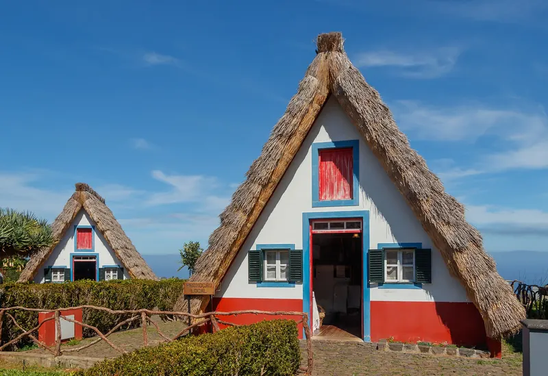 Casas típicas de Santana na Madeira — pequenas casas triangulares de colmo pintadas de branco, vermelho e azul, rodeadas por jardins floridos